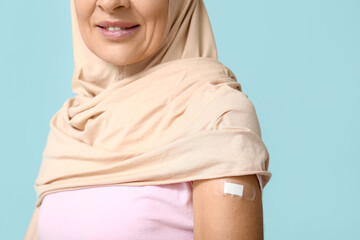 Mature Muslim woman with medical patch on arm against blue background. Vaccination concept