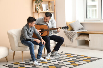 Happy father and his little son playing guitar on sofa at home