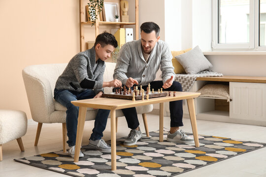 Father and his little son playing chess on sofa at home