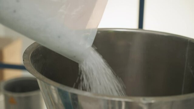 Pouring the huge amounts of plastic pellets into the metal container. Pouring the plastic pellets from the bag. Filling up the bowl by pouring lots of small plastic pellets. Close-up.