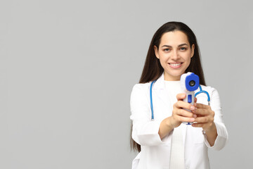 Portrait of female doctor with infrared thermometer on grey background