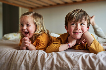 Happy siblings lying down on their bed, laughing and having fun.