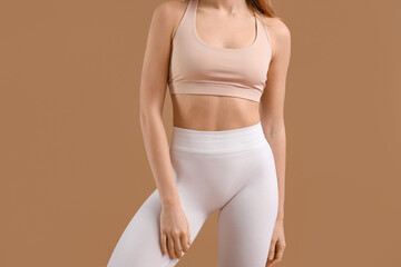 Beautiful young woman in sportswear on brown background, closeup