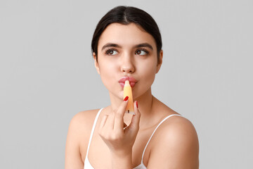 Beautiful young woman applying lip balm on grey background