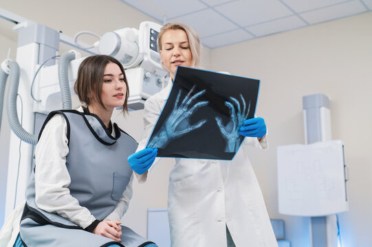 a female doctor and a young female patient look at an x-ray of hands, fingers and rejoice in the radiology room against the background of medical equipment. No bone fracture.	