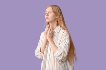 Beautiful young woman praying on purple background