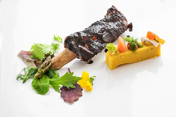 Glazed short rib with polenta, bean cream, vegetables and wild herb salad on a white plate, meat dish as main course in a gourmet menu, copy space, selected focus