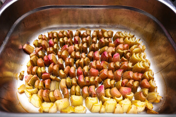 Diced rhubarb in a metal bowl prepared for cooking in the oven, healthy vegetarian dessert, selected focus