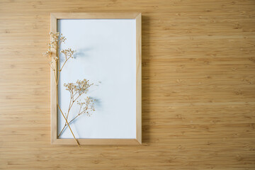 Small twig of gypsophila on an empty picture frame on a bamboo background, still life and home decor in minimalist Japandi style, background for products like cosmetics, copy space
