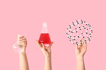 Female hands holding molecular model with filled flasks on pink background. Chemistry lesson concept