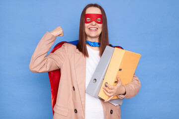 Confident strong smiling cheerful woman wearing superhero costume and mask holding folders isolated...