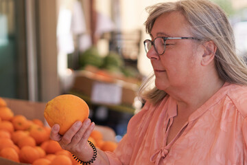older white-haired woman buying oranges at a street market