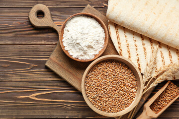 Tasty lavash, bowls with wheat grains and flour on wooden background