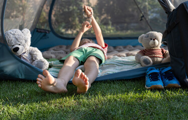 barefoot child is sleeping or relaxing while lying in a tent with his favorite teddy bear. Healthy...