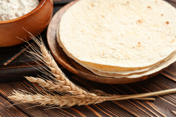 Tasty lavash and ear of wheat on wooden background, closeup