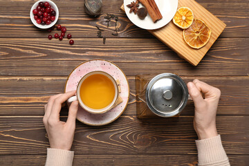 Female hands holding teapot and cup of fresh tea on wooden background