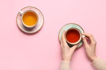 Female hands holding cup of black tea and cup of green tea on pink background