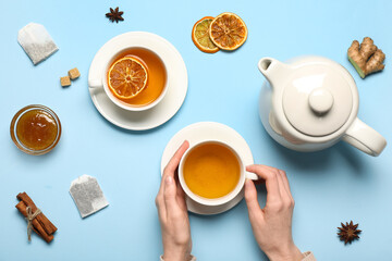 Female hands holding cup of fresh tea, teapot and jam on color background