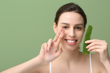 Beautiful young woman applying aloe vera with two fingers on green background
