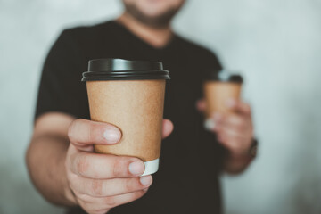 A man reaching out a brown hot coffee cup of coffee giving you. Would you like some coffee. Male bringing coffee