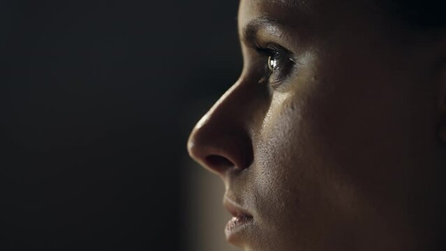 A woman face is shown in a dark room watching the favorite movie shot. The woman's eyes are wide open. Concept of mystery and introspection