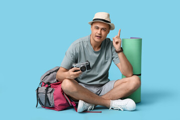 Young male tourist with photo camera pointing up on blue background