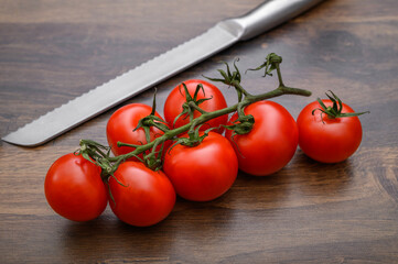 Duży stalowy nóż obok dojrzałych pięknych czerwonych pomidorów na gałązce leżą na blacie kuchennym  - obrazy, fototapety, plakaty