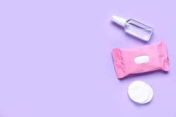 Cotton pads with bottle of sanitizer and wet tissues pack on purple background