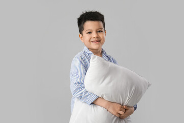 Cute little Asian boy in pajamas with pillow on white background