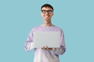 Young tattooed man in eyeglasses using laptop on blue background