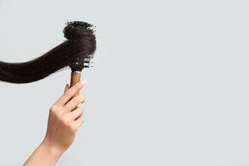 Beautiful young woman brushing her hair on grey background, closeup