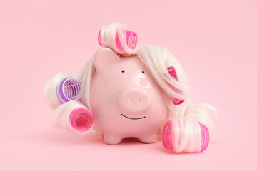 Piggy bank in wig with hair curlers on pink background