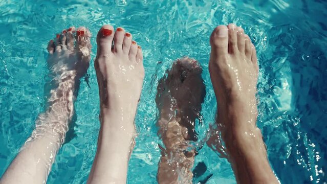 A man and a woman are in a pool with their feet in the water. Scene is relaxed and carefree, vacation concept, slow motion