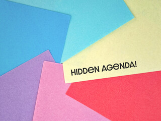 Hidden agenda text with multicolored paper background. Stock photo.