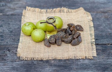 Amla Oil in a Glass Bottle or Indian Gooseberry Candy or Amla Fruit on Burlap Fabric Isolated on Wooden Background with Copy Space, Also Known as Emblica Myrobalan or Phyllanthus Emblica