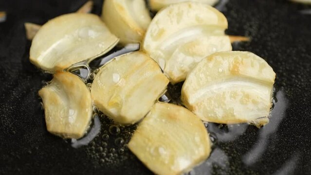 Frying garlic in oil in pan, close up
