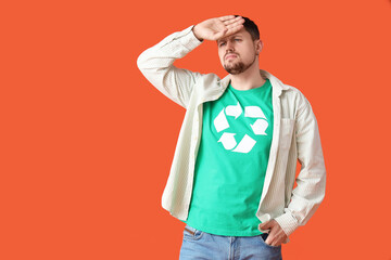 Confused young man in t-shirt with recycling logo looking at something on orange background....