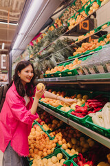 Young Korean woman shopping without plastic bags in grocery store. Vegan zero waste girl choosing fresh fruits and vegetables in supermarket. Part of a series