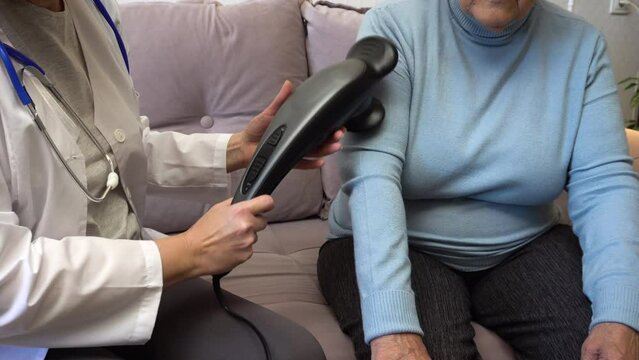 A home doctor massages an elderly woman's arm using an electric massager. Ideal for content about senior healthcare, senior health care, and home health care programs.
