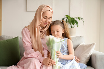 Little girl with her Muslim mother and tulips sitting on sofa at home