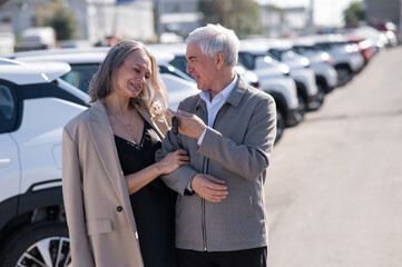 Mature Caucasian couple standing by a car outdoors. Elderly man holding car keys. 