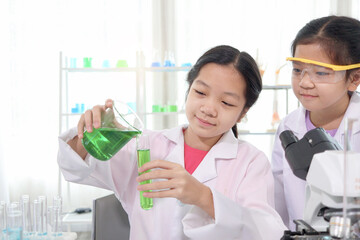 Cute young scientist schoolgirls in lab coat doing science experiments in laboratory.  Student girl child pouring green reagent solution from beaker into test tube. Kid learning science education. - Powered by Adobe