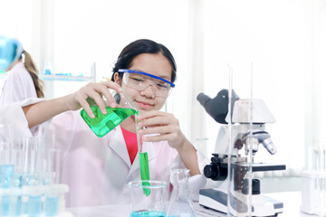 Cute young scientist schoolgirl wearing lab coat and safety glasses, doing science experiments....
