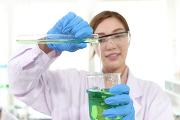 Hands of scientist woman in lab coats with safety glasses pouring chemical from test tube into...
