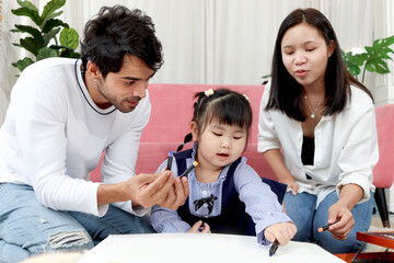 Happy Asian family. Chubby little girl daughter drawing together with father and mother in living room. Parents spend time with toddler kid at home. Child, mom and dad playing together in house.