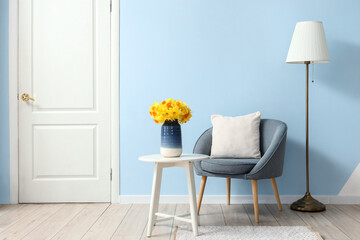 Armchair and coffee table with vase of narcissus flowers in blue living room