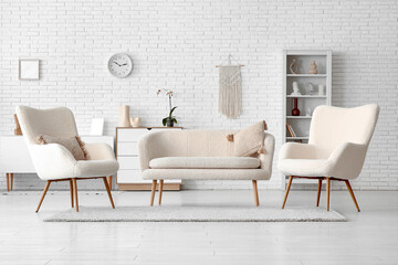 Interior of living room with sofa and armchairs against white brick wall