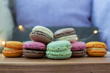 Close up delicious macaroon cookies in fresh mint green vanilla beige chocolate brown orange and pink colors. Dark gray background, wooden textured table. Contrast bright combination, bakery culinary.