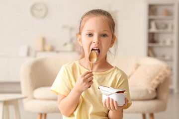 Cute little girl with spoon eating yogurt at home