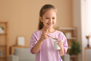 Cute smiling little girl eating yogurt at home
